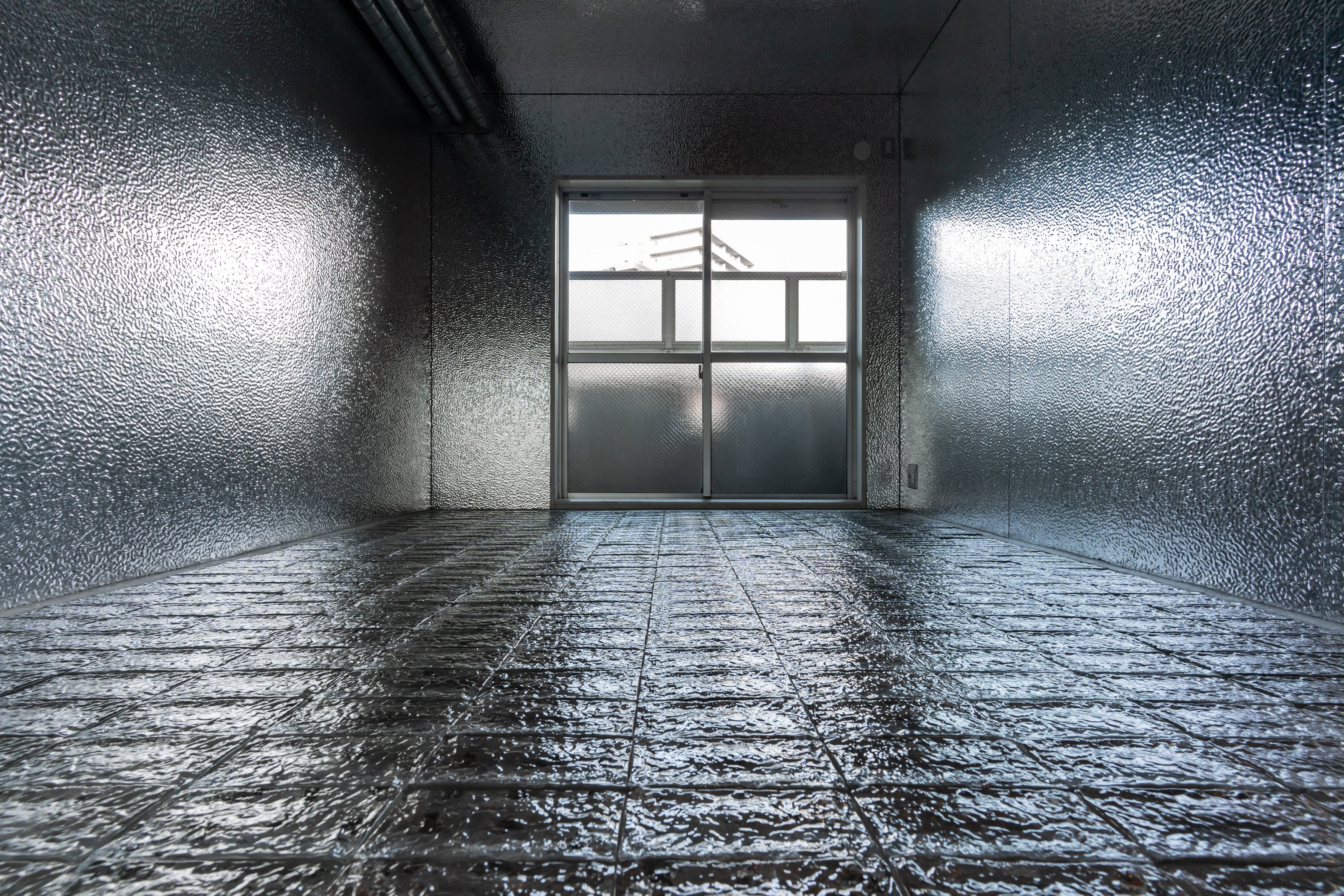 床にTHE GLASSを使用した無機質なインダストリアル空間。金属調の壁面とガラス床が光を反射する内装デザイン。