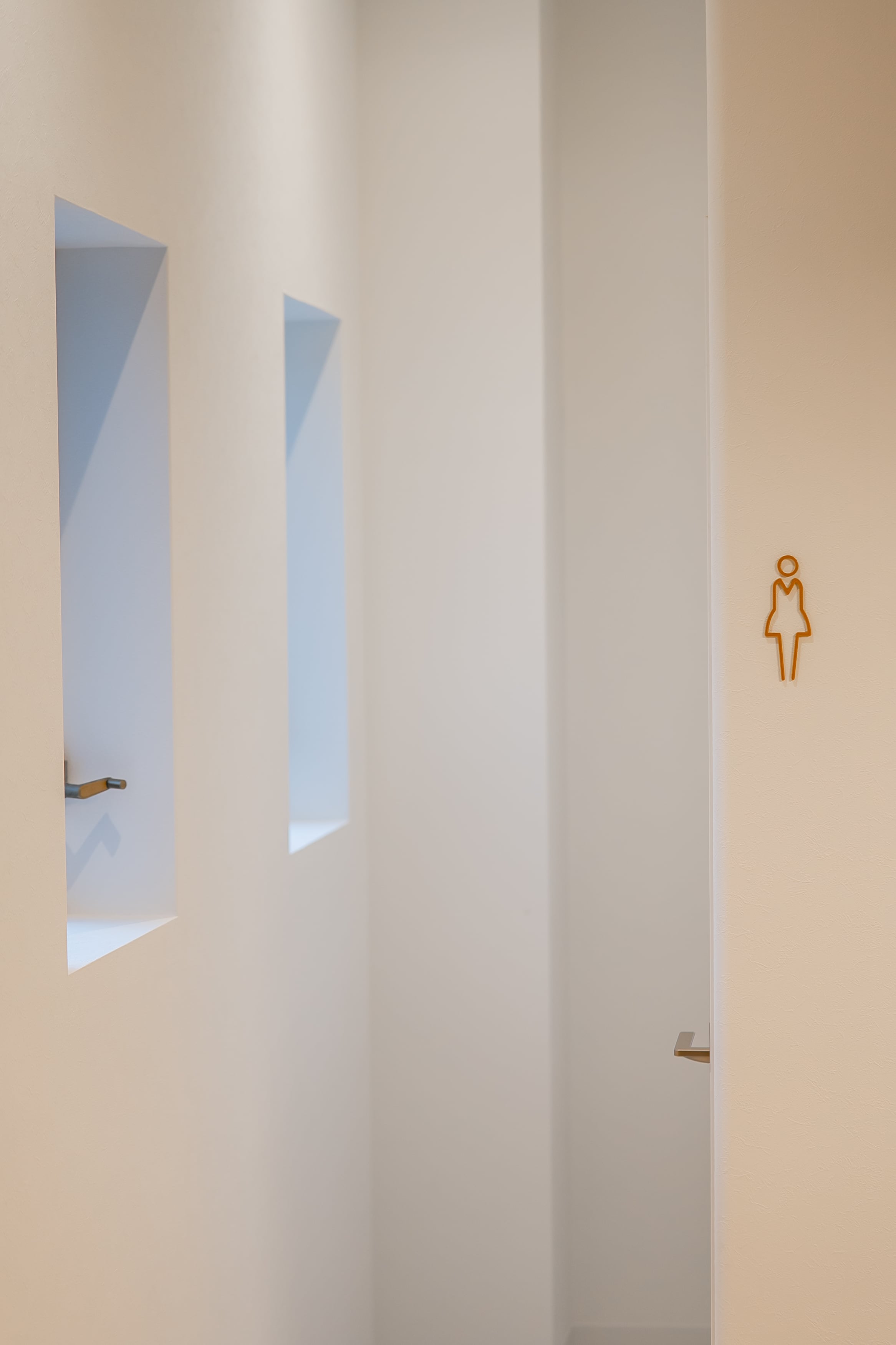 トイレの個室入口デザイン|白壁とアイコンサインの清潔な内装施工例